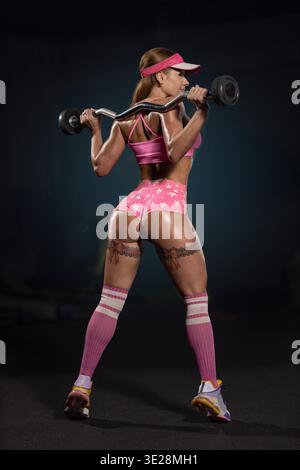 Sweaty athletic woman exercising with barbell, highlighting dedication and pink fitness attire in gym. Stock Photo