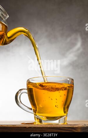 Glass cup of tea on wooden table with teapot filling Stock Photo