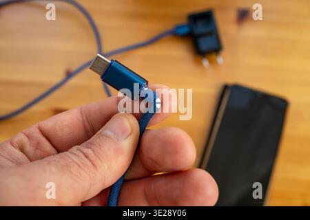 Male hand and fingers holding broken phone charging cable , soft focus Stock Photo
