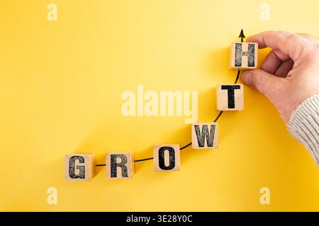 Male hand of a businessman placing wooden cubes with growth word written on a ascending arrow graph, on yellow Stock Photo