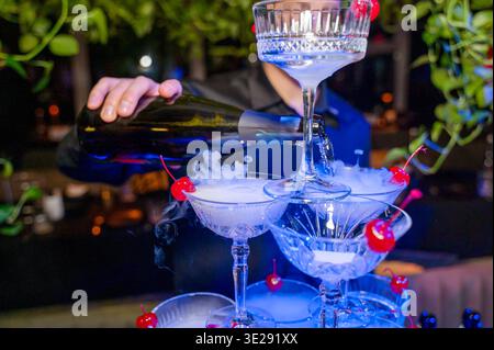 Close up of a hand filling a champagne pyramid with sparkling wine. The bottle is tilted over tiered crystal coupes at a party. Concept of luxury life Stock Photo