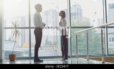 Two Caucasian business colleagues meeting in company hall talking successful businessman and businesswoman in office talk discuss negotiation work Stock Photo
