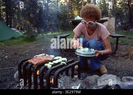 Glacier Point, Yosemite, USA – July 19, 1978: A young, unidentified woman is preparing tonight's dinner on a grill: T-bone steak and onions. Editorial Stock Photo