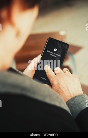 Fingerprint biometric authentication on smartphone. Senior woman unlocking phone with touch ID. Cybersecurity and digital inclusion concept. Stock Photo