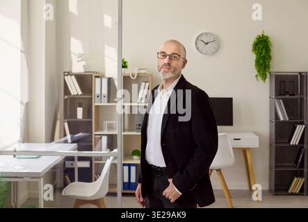 Confident middle aged businessman in glasses posing in modern office interior Stock Photo