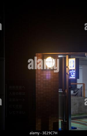 Nighttime urban parking entrance with lit wall lamp and neon sign on brick facade Stock Photo