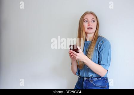 Woman using smartphone while standing near wall. Messaging, mobile app and modern digital lifestyle concept. copy space Stock Photo
