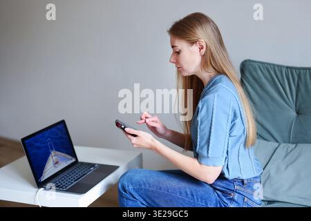 Happy woman sitting at desk with laptop and smartphone searching travel destinations online. Remote lifestyle concept. Stock Photo