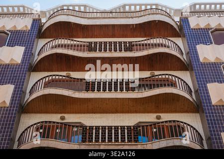 Low angle view of a modern apartment building facade featuring wavy wooden balconies, geometric tiles, and repeating architectural patterns for urban design and architecture concepts. Stock Photo