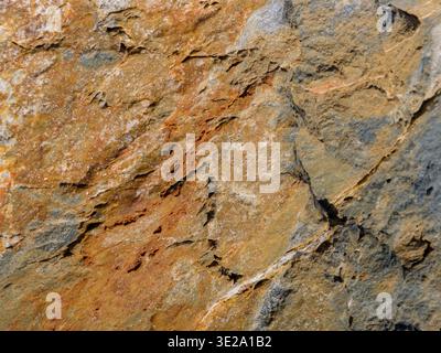 High resolution closeup of rough natural rock surface showing layered structure, cracks and warm earthy colors, useful as geology background, stone texture or design overlay. Stock Photo