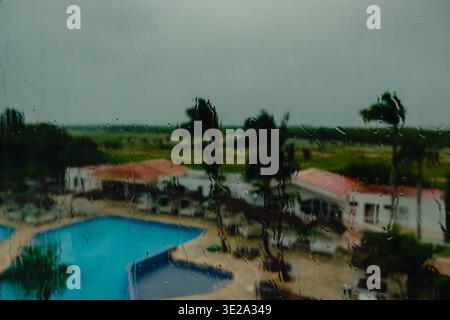 View of the pool and palm trees in the hotel through the window with raindrops. Abstract blurred background. Stock Photo