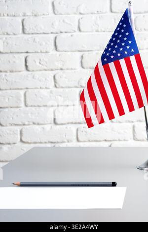 Small USA flag on a desk with a pencil and blank paper in a simple room setting Stock Photo