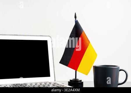 Small German flag next to laptop and mug on a desk Stock Photo