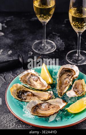 Opened fresh oysters on a blue plate, served with lemon and ice. Stock Photo