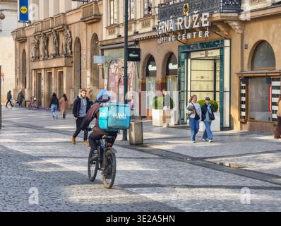 Prague, Czech Republic - March 19, 2026: Delivery courier on a bicycle in Prague historic center. Courier riding through cobblestone pedestrian street Stock Photo