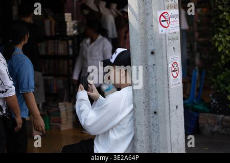 BANGKOK, THAILAND-MAR 1, 2026: Male tourist resting in market and using smartphone, daily smartphone activity, side profile, Chatuchak Market. Stock Photo