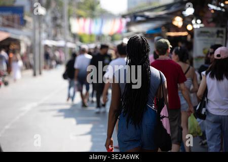 Female tourist with dreadlocks exploring outdoor market in Bangkok, budget shopping street market Asia, rear view. Stock Photo