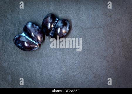 Two purple plums on a dark textured background. Close-up of two dark purple plums lying side by side on a dark textured surface. Top view. Free space Stock Photo