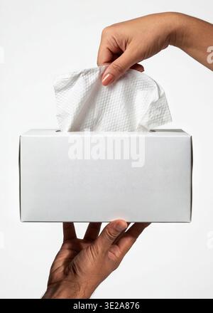 Mockup of a white rectangular tissue box, held by hands with a tissue being pulled out. Stock Photo