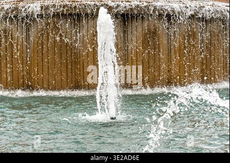 Fountain water jet shooting into a pool with cascading water over a textured wall Stock Photo