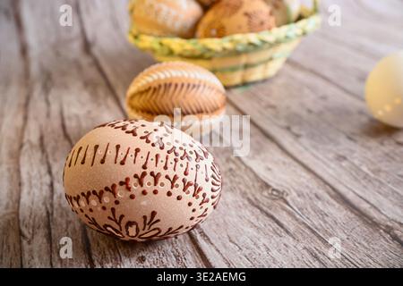 Easter eggs featuring intricate wax decorations on a wooden background with a basket. Stock Photo