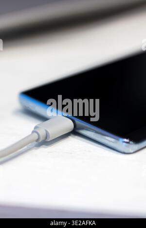 Closeup smartphone charging cable plugged in, sleek blueedge phone receiving power on clean white surface, soft studio Stock Photo