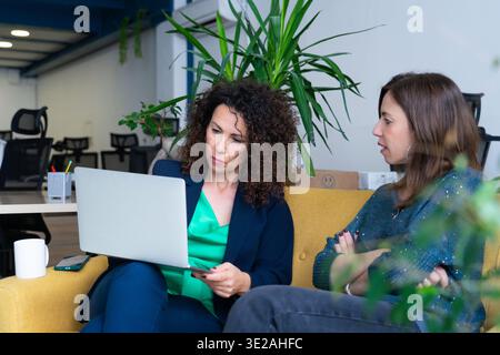 Two businesswomen collaborating on a project, using a laptop in a modern office environment Stock Photo