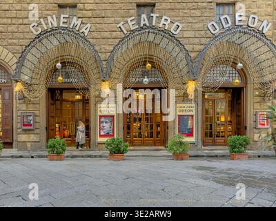 A woman looking at her phone outside the entrance to Giunti Odeon Liberia e Cinema, a cinema converted into a bookshop and cinema in Florence, Italy Stock Photo