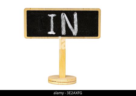 A miniature wooden stand holds a blackboard sign with handwritten chalk text reading IN, isolated on a clean white background with copy space for crea Stock Photo