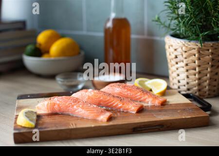 salmon fillets seasoned with sea salt crystals and cracked black pepper, arranged on a two-tone wooden cutting board with lemon wedges. Stock Photo