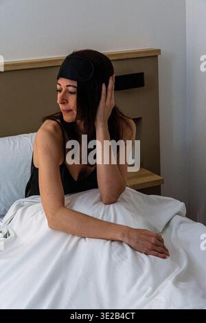 Woman waking up in bed wearing sleep mask Stock Photo
