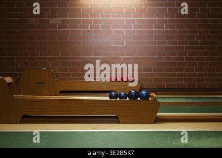Interior view of a classic bowling alley with wooden track, green playing area and red and blue balls on a ball slide in front of a brick wall, German Stock Photo