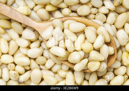 Top view of wood spoon with shelled pine nuts on pile of nuts close up Stock Photo
