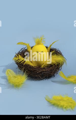 Cute yellow Easter eggs in the shape of chicks surrounded by feathers on a bright blue background. Easter greeating card Stock Photo