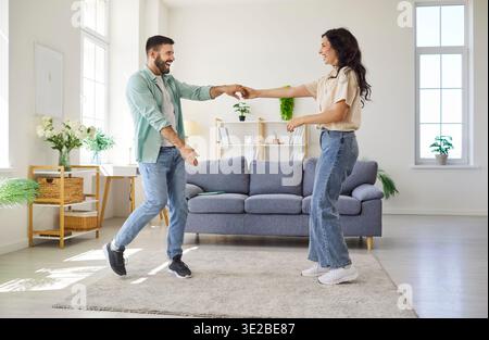 Happy couple dancing together at home, holding hands with joy in living room Stock Photo