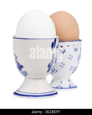 Side view of pair of boiled eggs in ceramic egg cups isolated on white background, the white egg on foreground Stock Photo