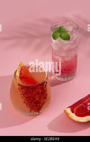 Two cold and refreshing cocktail with ice garnished grapefruit slice and mint stands on pink background. Summer non-alcoholic cocktails with juice and Stock Photo