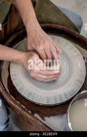 Woman working on the potter's wheel. Ceramist young woman making clay product on pottery lathe in studio. Close up of female hands working on potters Stock Photo