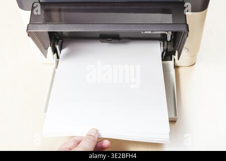Putting of white paper sheets in printer tray of multi function device on table in office Stock Photo