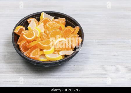 Sweet sugar lemon and orange marmalade slices in ceramic bowl on gray wooden table Stock Photo