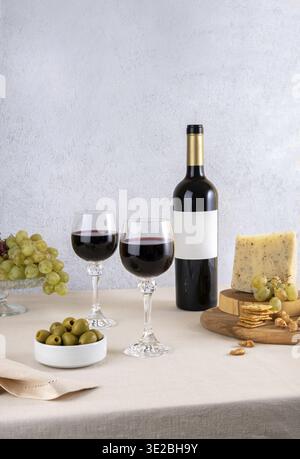 Glass and bottle of red wine with blue cheese and grapes on light background. Red wine with cheese and fruits. Wine bottle mockup with blank labels to Stock Photo