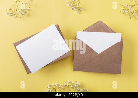 Blank greeting cards and envelopes with gypsophila on yellow background. Blank paper sheet cards with mockup copy space. Minimal workplace composition Stock Photo