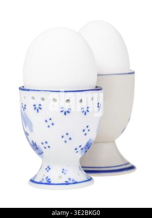 Side view of pair white boiled eggs in ceramic egg cups isolated on white background, the egg with a pointy end up on foreground Stock Photo