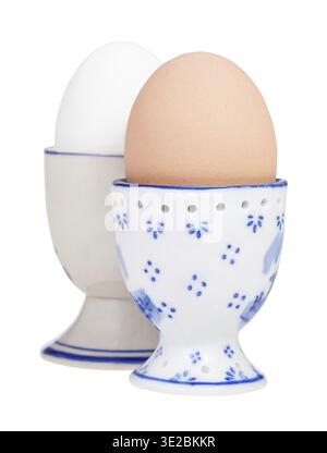 Side view of two boiled eggs in ceramic egg cups isolated on white background, the brown egg on foreground Stock Photo