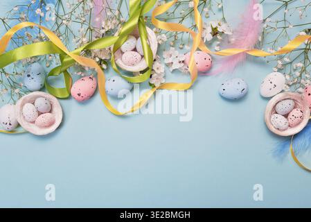 Flat lay of Easter eggs, decorative nests, and blue feathers on pastel blue background, greeting card concept with festive spring design Stock Photo