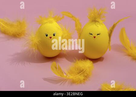 Cute yellow Easter eggs in the shape of chicks surrounded by feathers on a bright pink background. Easter greeating card Stock Photo