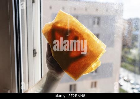 Male hand wipes dirty outdoor side of window glass with rag in multi-storey city house on sunny spring afternoon Stock Photo