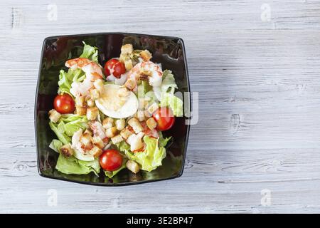 Top view of Caesar salad with prawns in black bowl on gray wooden table with copyspace Stock Photo