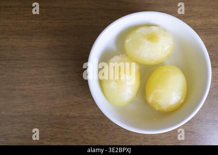 Top view of three peeled raw frozen eggs in bowl on brown table Stock Photo