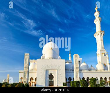 A mosque in Abu Dhabi features large domes and a tall minaret against a clear blue sky. People visit the site to admire its design. Stock Photo